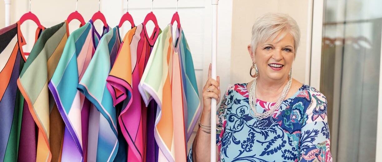Donna Rowland next to a rack of bright and beautiful clothes