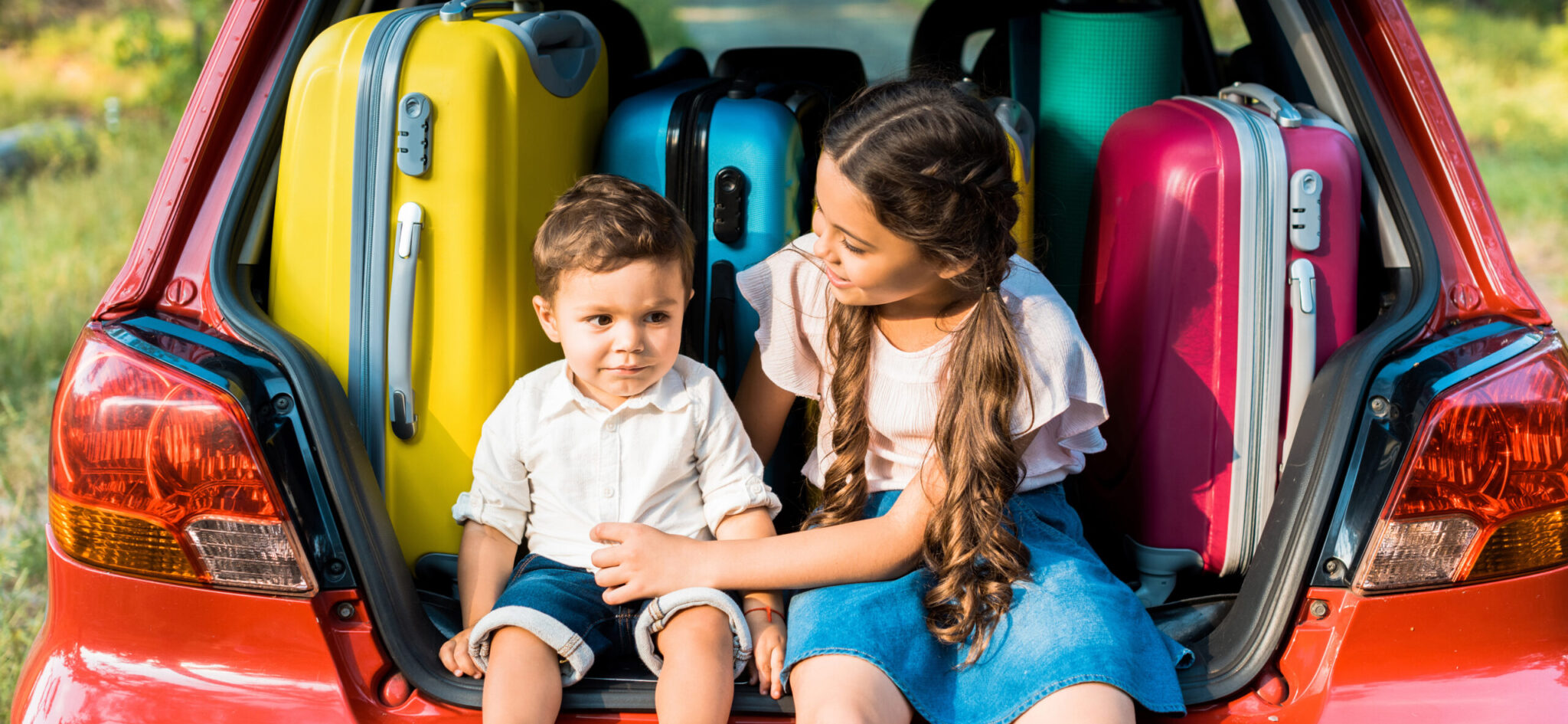 Picture of little girl and little boy in the back of a car in front of suitcases